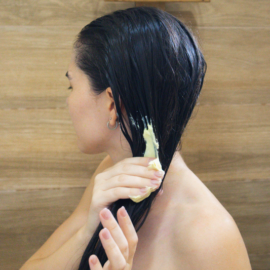 Mujer aplicando mascarilla capilar en el cabello mojado dentro de la ducha